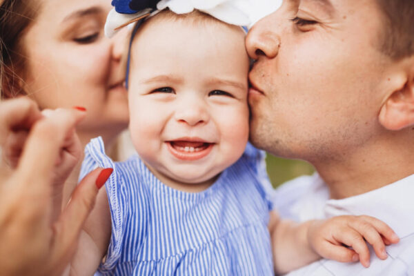Two parents kissing their happy baby