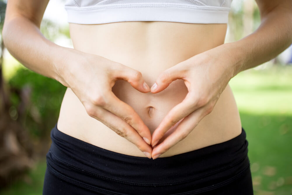 A woman making a heart shape over her stomach